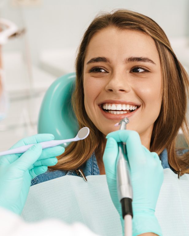 European smiling woman sitting in medical chair while dentist fixing her teeth at dental clinic