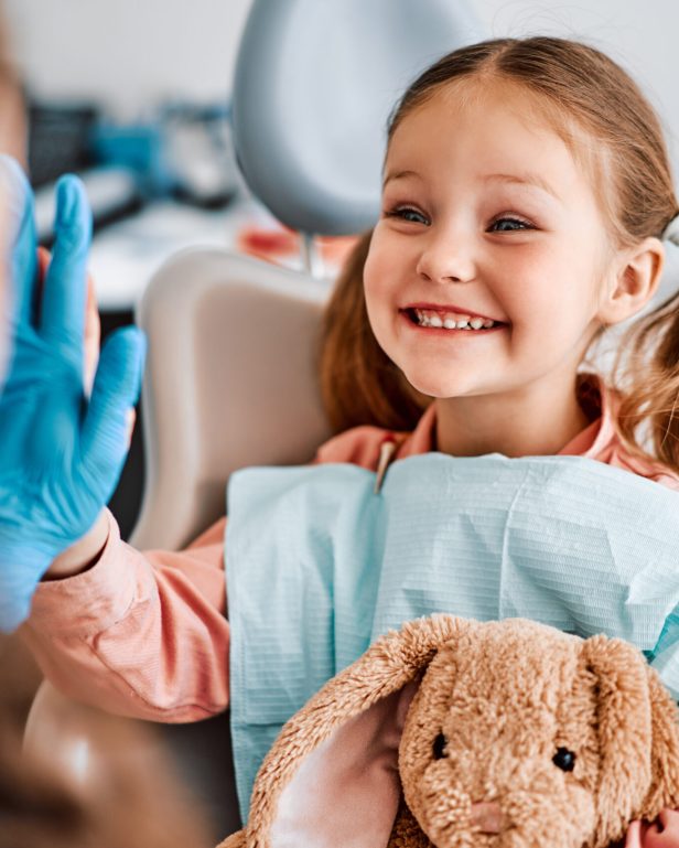 At the doctor's appointment. A candid emotional photo of a child sitting in a dental chair, holding a toy rabbit and cheerfully giving a high-five to the nurse.